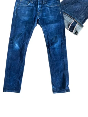 Edwin Japansk selvedge denim  - Klassiska selvedge jeans från edwin med raka ben och femficksmodell. Jeansen har tydliga kontrastsömmar och den ikoniska Edwin-detaljen på bakfickorna. Tillverkade i slitstark denim med uppvikbar kant som visar rå denim på insidan.