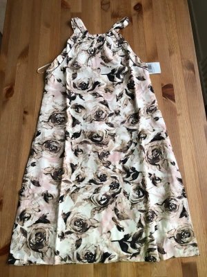 Blommig kortklänning från Mango - Snygg kortklänning från Mango med blommigt mönster i beige, brunt och ljusrosa toner. Klänningen har ärmlös design med smala axelband och en lätt A-linjeform. Perfekt för varma dagar och somriga tillfällen.