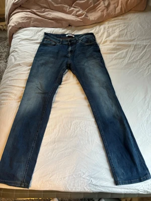 Blå bootcut jeans från Tommy Jeans - Säljer ett par klassiska blå bootcut jeans från Tommy Jeans. Jeansen har fem fickor. Storleken är W31/L34. Dem är i bra skick men jag säljer för att jag upplevde dem lite för tajta för min smak. Bra kap för pengarna. Jag är 180cm 80kg på bilden. 
