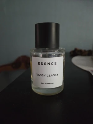 ESSNCE Sassy Classy Eau de Parfum - ESSNCE Sassy Classy Eau de Parfum i en stilren, rund glasflaska med svart lock. Parfymen har en minimalistisk vit etikett med svart text. Perfekt för dig som gillar en modern och enkel design.