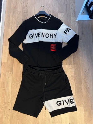 Svarta och vita shorts från Givenchy - Snygga svarta shorts från Givenchy med vit panel och svart text. Shortsen har elastisk midja med snörning och en röd Givenchy-logga på sidan. Perfekta för en trendig och avslappnad stil.