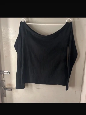 off shoulder tröja  - Svart ribbad tröja med off shoulder-modell och långa ärmar. Tröjan är tillverkad i mjukt material. Perfekt för en avslappnad och trendig look.