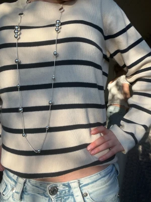 Beige randig tröja med svarta ränder - Snygg beige tröja med svarta horisontella ränder. Tröjan har rund halsringning och långa ärmar. Perfekt för en avslappnad och trendig look. Materialet ser ut att vara mjukt och bekvämt, passar bra till jeans.