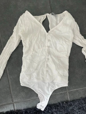 Vit långärmad body med knappar - Säljer denna jätte söta body från Hollister då den är för liten för mig. Den har knappar där fram och super sött mönster. Perfekt för sommar och våren!🥰