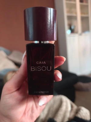 CAIA Bisou Eau de Parfum - Snygg parfymflaska från CAIA i modellen Bisou. Flaskan är mörklila med en stilren, fyrkantig form och ett matchande lock. Parfymen är Eau de Parfum och flaskan är tillverkad i glas med metalliska detaljer. Perfekt för dig som gillar trendiga och eleganta dofter. 50ml. Är ca 2/5 kvar 