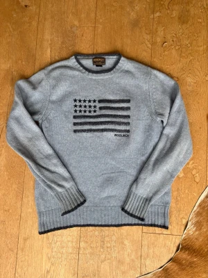 Woolrich stickad tröja - En jättefin stickad tröja med usa flaggan från woolrich. Tröjan är i fint skicka och har inga större defekter. Den är S och passar dig som är ca 170cm. Tveka inte att skriva vid frågor och priset kan diskuteras