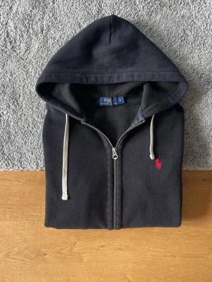 Svart hoodie från Polo Ralph Lauren - Svart Ralph Lauren hoodie med dragkedja i storlek S säljes. I mycket bra skick och utan defekter. Stilren och bekväm zip hoodie som passar perfekt till vardags.  ✅ Storlek S ✅ Dragkedja ✅ Mycket bra skick ✅ Inga defekter ✅ Snabb frakt  Hör gärna av er vid frågor eller om ni vill ha fler bilder!