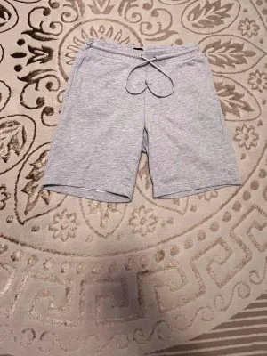 Grå mjukisshorts från H&M - Gråa mjukisshorts från H&M med relaxed fit och snörning i midjan. Perfekta för chill dagar eller träning. Tillverkade i mjuk bomullsmix för extra komfort och har en enkel, stilren design.