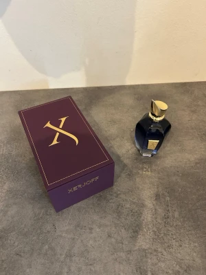 Xerjoff More Than Words perfume - Lyxig parfym från Xerjoff i en elegant mörkblå glasflaska med gulddetaljer och unik, skulptural kork. Kommer i en stilren lila ask med guldfärgad logotyp. Perfekt för dig som gillar exklusiva dofter och snygg design.