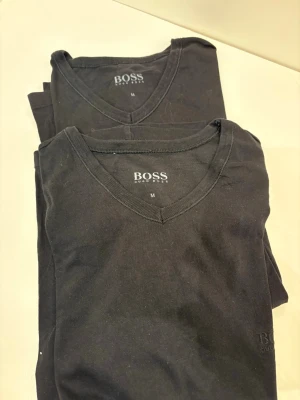 2 Svarta t-ashirt från BOSS - Säljer en klassisk svart t-shirt från BOSS med v-ringad hals. Tillverkad i mjuk bomull som känns skön mot huden. Perfekt basplagg med stilren design och diskret logga på bröstet. Passar till allt och är enkel att matcha. 2 för 69