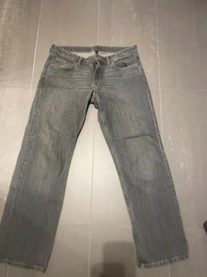 Grå raka jeans från Arrow - Säljer ett par grå jeans från weekday ”arrow low”  med rak passform och klassisk femficksdesign. Jeansen har snygga kontrastsömmar och är tillverkade i ett slitstarkt denimtyg. Perfekta för dig som gillar en avslappnad och tidlös stil. Midjemått rakt över ca 41 cm. Innerbenslängd ca 73 cm