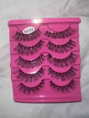 Fempar lösögonfransar i svart - Säljer ett set med fem par dramatiska lösögonfransar i svart. Fransarna har en fyllig och fluffig design med varierande längd för en intensiv look. De kommer i ett rosa plastetui och är perfekta för att framhäva ögonen. Helt nya och oanvända