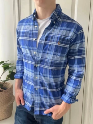 Blå rutig skjorta från Ralph Lauren S - Säljer en blå rutig skjorta från Ralph Lauren med klassisk button-down krage och broderad logga på bröstet. Skjortan har långa ärmar, vita knappar och är tillverkad i mjuk bomull. Perfekt för en avslappnad men ändå stilren look. Denna modellen säljs inte längre men går att hitta en liknande för ~2300 kr på Ralph Laurens hemsida. Mycket fint skick utan defekter. Modellen är 182 cm 70 kg. Hör av er vid frågor och funderingar!