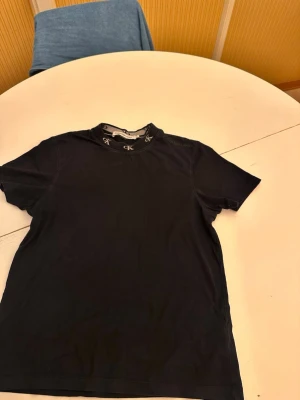 Svart t-shirt från Calvin Klein Jeans - Snygg svart t-shirt från Calvin Klein Jeans med diskret logga på bröstet och 'ck' broderat runt halsringningen. Klassisk passform och rund hals. Perfekt till jeans eller shorts för en clean och stilren look.