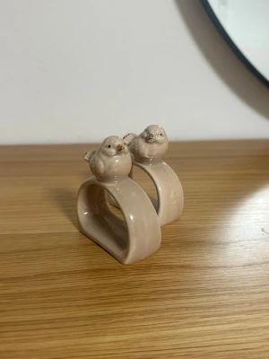 Beige ringar med fåglar i keramik - Två unika ringar i beige keramik med söta små fåglar på toppen. Ringarna har en fyrkantig form och en glansig finish som ger dem en modern och lekfull känsla. Perfekt accessoar för dig som gillar detaljer med djurmotiv.