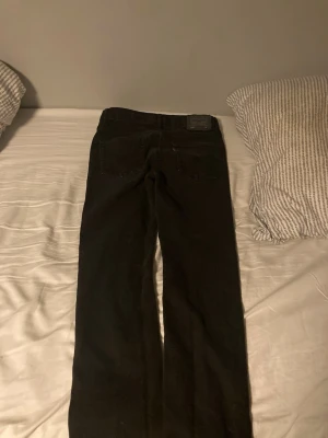 Svarta raka jeans från Levi's - Säljer ett par svarta jeans från Levi's med klassisk rak passform och femficksdesign. Jeansen har en diskret logotyp på bakfickan och är tillverkade i ett robust denimtyg. Perfekta för dig som gillar en tidlös och clean stil.