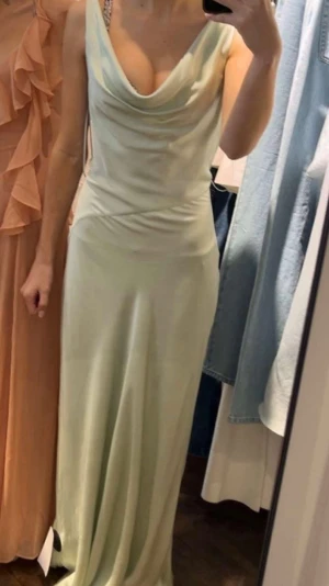 Ljusgrön långklänning i satinlook - Säljer en elegant ljusgrön balklänning i satin med draperad urringning och drapering i ryggen också. . Klänningen har en fin passform och faller snyggt längs kroppen. Köpt från twist and tango för 2400 kr. Aldrig buren och lappen sitter kvar.