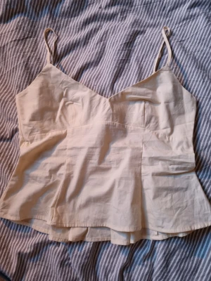 Gul linnetopp med smock och tunna band - Snygg gul linnetopp med tunna axelband och smockad rygg för extra komfort. Toppen har en lätt utsvängd passform och är tillverkad i mjuk bomull, perfekt för varma dagar. Enkel och stilren design som passar till det mesta.