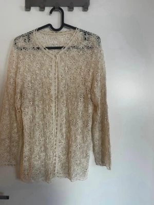 Beige spetskofta med blommönster - Säljer en tunn och elegant beige kofta i spets med detaljerat blommönster. Koftan har långa ärmar och knäppning framtill. Perfekt för att lyfta en outfit med en romantisk touch. Handgjord. Rök och djurfritt hem. Pruta gärna !🌸