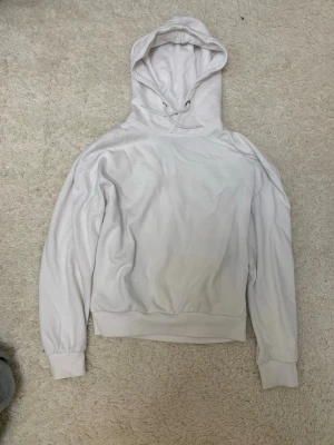 Vit hoodie med huva och dragsko - Säljer en enkel vit hoodie med huva och dragsko. Hoodien har ribbade muddar vid ärmslut och midja, samt en klassisk passform. Perfekt för en avslappnad stil. Materialet känns mjukt och bekvämt.