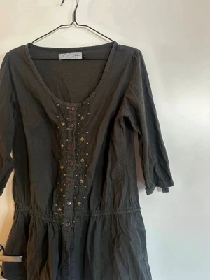 Grå blus med dekorativa knappar - Snygg grå blus med trekvartsärm och rund halsringning. Framsidan har dekorativa knappar och guldfärgade nitar i ett mönster längs knappslån. Blusen har en avslappnad passform och lätt rynkad midja. Perfekt för dig som gillar detaljer och en unik look. Rök och djurfritt hem. Pruta gärna !🌸