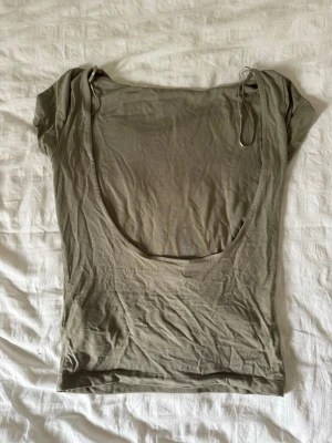 Beige croppad topp med öppen rygg - Trendig beige croppad topp med korta ärmar och en djup öppen rygg. Tillverkad i mjuk bomull som känns skön mot huden. Perfekt för dig som vill ha en enkel men snygg bas i garderoben.