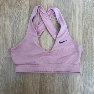 Rosa sport-bh Nike - Säljer en ljusrosa sport-bh från Nike med korsade axelband i ryggen och diskret Nike-logga framtill. Perfekt för träning och har bred resår nedtill för extra stöd. Snygg och bekväm modell.Pris 50kr.
