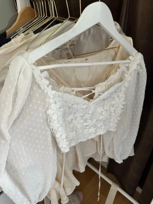 Vit blus med spets och puffärmar - Supersöt vit blus med blommig spets framtill och transparenta puffärmar med diskreta prickar. Toppen har snörning i ryggen.