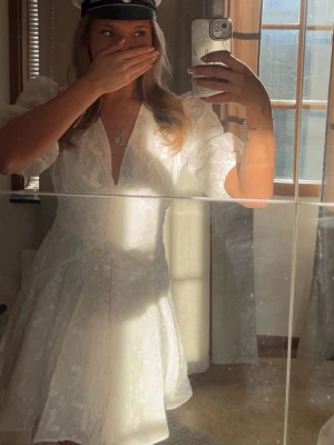 Vit Adoore klänning  - Säljer min supersöta studentklänning med puffärmar och djup v-ringning från Adoore. Klänningen har knappar framtill och blommigt mönster i tyget. Perfekt till student eller sommarens alla tillfällen. Köpte den helt ny och endast använd en gång så väldigt bra skick och inga märken på slitage. 