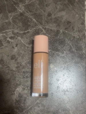 e.l.f. Halo Glow Liquid Filter foundation - e.l.f. Halo Glow Liquid Filter foundation i en beige nyans. Kommer i en cylinderformad glasflaska med ljusrosa lock och vit text. Ger en glowig finish och är perfekt för dig som vill ha en naturlig lyster. Flytande formula som är lätt att applicera. Har använt den två till tre gånger men insåg att den va för ljus 
