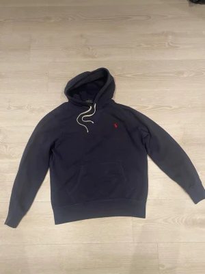 Mörkblå hoodie från Polo Ralph Lauren - Snygg mörkblå hoodie från Polo Ralph Lauren med klassisk röd logga broderad på bröstet. Fint skick på tröjan, bara att höra av dig vid någon fundering!