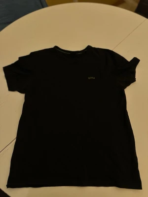 Svart t-shirt från BOSS - Snygg svart t-shirt från BOSS med diskret logga på bröstet. Klassisk rund halsringning och korta ärmar. Tillverkad i mjuk bomull som känns skön mot huden. Perfekt basplagg för en clean och stilren look.