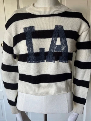 Randig stickad tröja med LA-tryck - Snygg stickad tröja med svarta och vita ränder samt stort LA-tryck framtill i mörkblått. Tröjan har rund halsringning, ribbade muddar och avslappnad passform. Säljer pga att den inte passar riktigt och storleken kan upplevas som xxs/xs💓