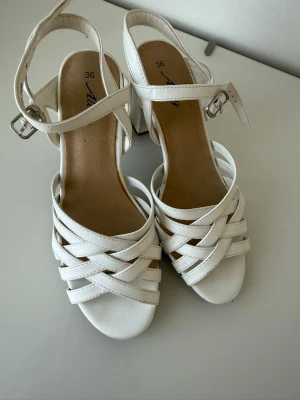 Vita sandaletter med blockklack - Snygga vita sandaletter från Axelda med flätade remmar och justerbart ankelband med spänne. Skorna har en stabil blockklack och öppen tå. Tillverkade i konstläder med mjuk innersula för extra komfort. Perfekta för sommarens alla outfits och speciellt till midsommar☀️☀️💕💕