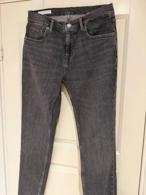 Grå raka jeans med fem fickor - Storlek S,  Säljer ett par grå jeans med klassisk femficksmodell och raka ben. Jeansen har bälteshällor, knappgylf och subtil tvättad look. Perfekta till en avslappnad stil och passar till det mesta. Materialet är denim i bomull.