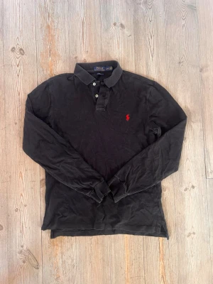 Svart långärmad piké från Polo Ralph Lauren - Klassisk svart långärmad pikétröja från Polo Ralph Lauren med röd broderad logga på bröstet.  Large passar medium
