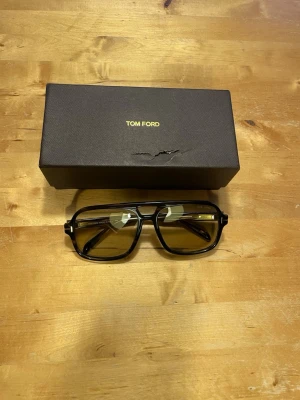 Tom Ford bruna solglasögon pilot - Snygga solglasögon från Tom Ford med klassisk pilotform. Bågarna är bruna med transparent känsla och glasen har en gul ton. Kommer med originaletui i svart med guldfärgad logga. Perfekt accessoar för dig som vill sticka ut.