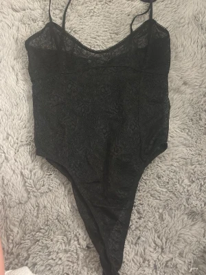 Svart spetsbody från Zara - Säljer en svart body från Zara i storlek S. Bodyn är tillverkad i tunn spets med smala axelband och v-ringad hals. Materialet är genombrutet och ger en elegant look. Perfekt att styla under en skjorta eller kavaj.