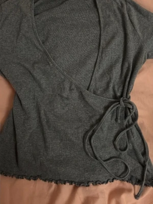 Grå omlottopp med knyt - Supersnygg grå topp med knyt i sidan och vågig kant nertill , stretchigt material som känns skönt mot huden. ‼️pris kan diskuteras 