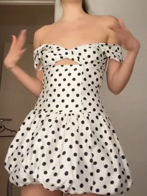 Vit prickig offshoulder kortklänning - Supersöt vit kortklänning med svarta prickar och offshoulder-design. Klänningen har en ballongformad kjol, cut-out detalj vid bysten och ärmlös look med volangkant. Perfekt för dig som vill sticka ut med en lekfull och trendig stil.