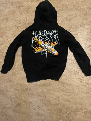 Jacker hoddie ”Crash” - En svart hoddie i märket Jacker storlek M. Trycket på baksidan föreställer ett kraschande plan i lågor.