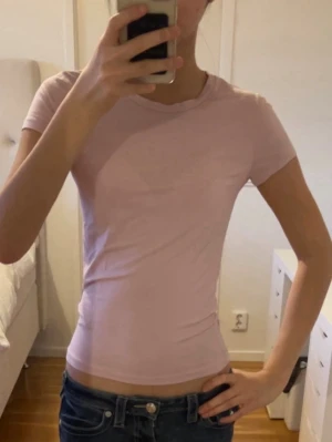 Ljusrosa basic t-shirt från Gina tricot - En enkel och stilren ljusrosa t-shirt från Gina tricot. Modellen är tight och har korta ärmar samt rund halsringning. Perfekt att matcha med jeans eller kjol för en clean look. Tillverkad i mjuk bomull som känns skön mot huden.