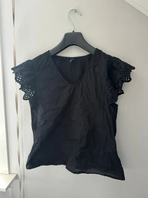 Svart blus med spetsärmar från ONLY - Säljer en svart blus från ONLY med v-ringning och korta, breda spetsärmar som ger en romantisk vibe. Toppen är i ett lätt material och har en lös passform. Perfekt att styla med jeans eller kjol för en trendig look.
