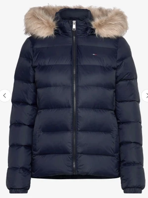 Svart Tommy hilfiger pufferjacka med fuskpäls - Snygg svart pufferjacka från Tommy Hilfiger med avtagbar huva och fuskpäls. Jackan har diskret logga på bröstet, dragkedja framtill och quiltad design. Perfekt för kalla dagar och ger en riktigt trendig look. Jackan ligger i förrådet, bild på den kan jag skicka privat 