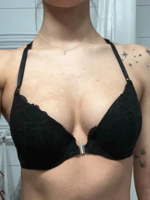 Svart spets-bh med racerback - Snygg svart bh med spetsdetaljer och vadderade kupor. Bh:n har en racerback i spets och knäpps framtill med ett metallspänne. Axelbanden är justerbara och designen ger ett elegant intryck.