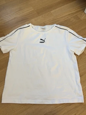 Y2K- 2000- talsstil Vit Puma t-shirt  - Snygg vit t-shirt från Puma med svart logga på bröstet och svarta linjer längs axlarna. Klassisk passform och rund halsringning. Perfekt till en avslappnad stil och enkel att matcha med jeans eller shorts.