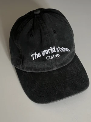 Grå keps - Säljer en grå keps med böjd skärm och broderad text som är använd ett fåtal gånger. Kepsen har klassisk sexpanelsdesign och justerbar rem bak. Materialet är mjukt och ger en avslappnad streetwear-vibe.