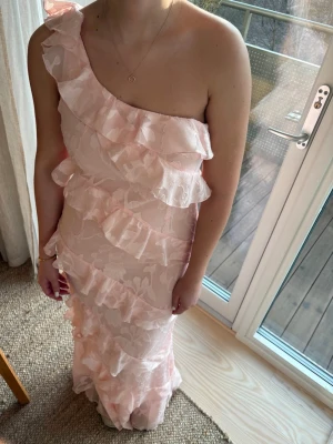 Rosa balklänning med volanger - Säljer denna superfina rosa klänningen med volanger samt one-shoulder, endast använd en gång! 🌸   Modellen på bilden är 1,75 cm lång!  Perfekt för alla tillfällen: bal, bröllop, fest, midsommar eller student!🌟  Storlek: på lappen står det UK 14 / EU 42 / US 10 (men klänningen är liten i storleken så passar mig som oftast bär M/L) Märke: Boohoo Skick: Mycket fint skick (som ny, endast använd en gång)  Hör av dig om du har några fler frågor!💖  📦 Postar snabbt
