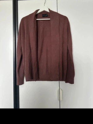 Rosa kofta från Black Story - Mysig öppen kofta i dammigt rosa från Black Story. Koftan har lång ärm, avslappnad passform och ribbade detaljer vid kragen. Perfekt att slänga över en topp för en chill look.