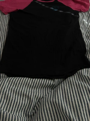 Svart t-shirt med rosa ärmar - Snygg t-shirt med svart kropp och kontrasterande rosa korta ärmar. Klassisk rund halsringning och enkel design som passar till det mesta. Perfekt för dig som gillar en sportig och avslappnad stil.